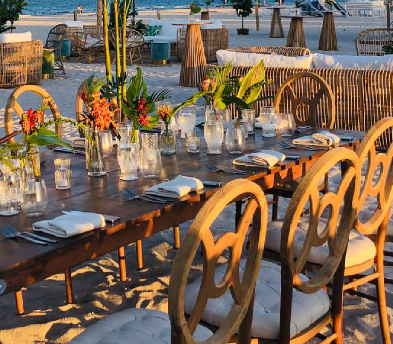 A golden-hour dinner table dressed with flowers and candles, set on the sand.