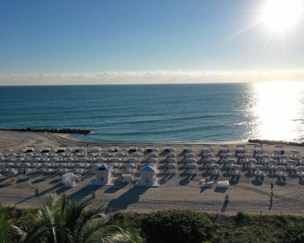 Rows of white cabanas and umbrellas along the shoreline under a rising sun.