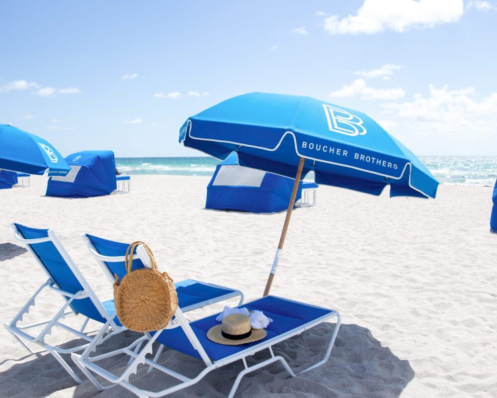 A pair of reserved loungers under a Boucher Brothers umbrella facing a quiet morning sea.